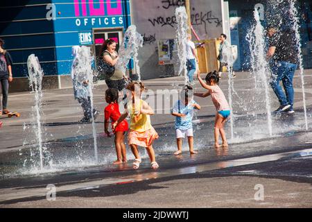 Wien, Österreich - 06.13.2022: Kinder tummeln sich in der Sommerhitze in den Jets des Stadtbrunnens Stockfoto