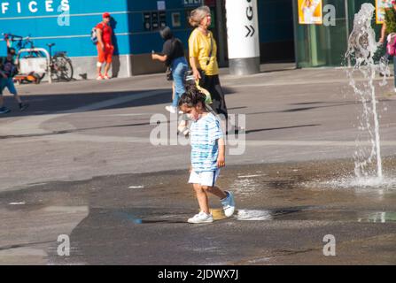 Wien, Österreich - 06.13.2022: Kinder tummeln sich in der Sommerhitze in den Jets des Stadtbrunnens Stockfoto