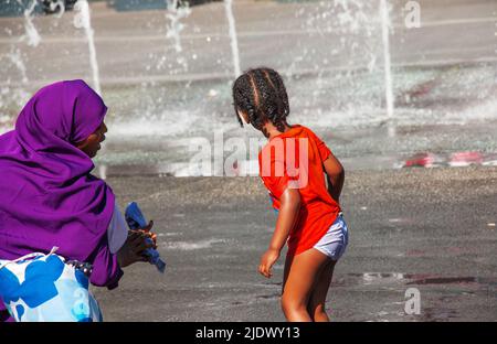 Wien, Österreich - 06.13.2022: Kinder tummeln sich in der Sommerhitze in den Jets des Stadtbrunnens Stockfoto