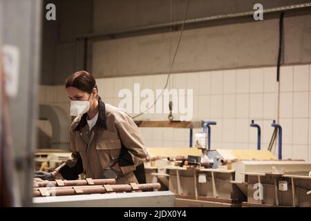 Beschäftigt Brünette Frau in Atemschutzmaske stehen in staubigen industriellen Werkstatt und Untersuchung verarbeitete Schläuche Stockfoto