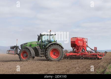 Ein Fendt-Traktor, der einen roten Bohrer zieht und sich am Ende des Feldes dreht, in dem er sät Stockfoto