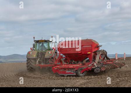 Ein grüner Fendt-Traktor mit einem roten Horsch-Sämaschine, der sich während der Aussaat von Gerste im Frühjahr am Rand eines gepflügten Feldes dreht Stockfoto