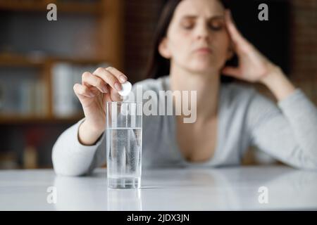 Verärgerte junge Frau, die unter Kopfschmerzen leidet, mit löslichem Medikament zur Schmerzlinderung. Erschöpfte Frau mit schmerzhaften Empfindungen. Migräne, hoher Blutdruck Stockfoto