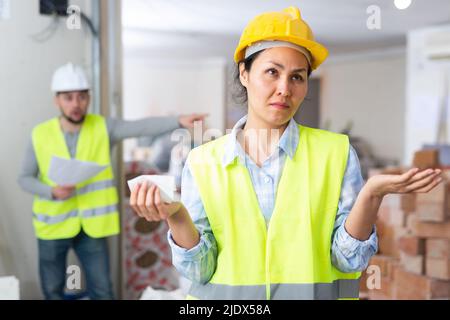 Verwirrte Ingenieurin und schreiender Vorarbeiter auf der Baustelle Stockfoto