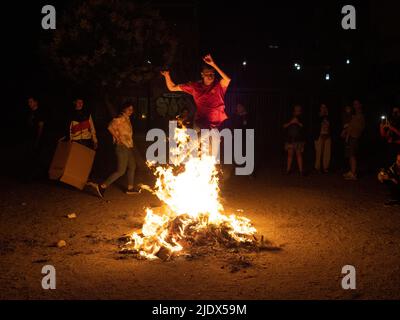 Madrid, Spanien. 23.. Juni 2022. Ein Mann, der während der Johanniternacht in Madrid durch das Feuer eines Lagerfeuers springt. Hunderte von Menschen feierten die Sommersonnenwende, indem sie Lagerfeuer im Cornisa Park während der Johannisnacht in Madrid anzünden. Die Leute verbrannten früher Papierstücke, die mit Dingen geschrieben waren, die man vergessen sollte, und hüpften sich über die Lagerfeuer, um Wünsche zu erfüllen. © Valentin Sama-Rojo/Alamy Live News. Stockfoto