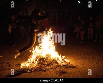 Madrid, Spanien. 23.. Juni 2022. Eine Frau, die während der Johanniternacht in Madrid durch das Feuer eines Lagerfeuers springt. Hunderte von Menschen feierten die Sommersonnenwende, indem sie Lagerfeuer im Cornisa Park während der Johannisnacht in Madrid anzünden. Die Leute verbrannten früher Papierstücke, die mit Dingen geschrieben waren, die man vergessen sollte, und hüpften sich über die Lagerfeuer, um Wünsche zu erfüllen. © Valentin Sama-Rojo/Alamy Live News. Stockfoto