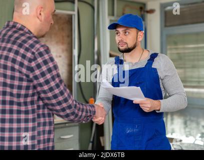 Mann hält Papiere und schüttelt die Hand mit dem jungen Baumeister Stockfoto