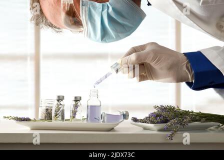 Wissenschaftler entwickeln ein Produkt mit Lavendelessenz in Glasfläschchen auf einer Werkbank. Vorderansicht. Horizontale Zusammensetzung. Stockfoto