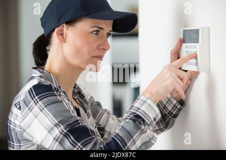 Frau, die den Thermostat an der weißen Wand anpasst Stockfoto