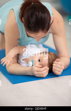 Mutter macht Plank-Übung über ihrem Baby Stockfoto