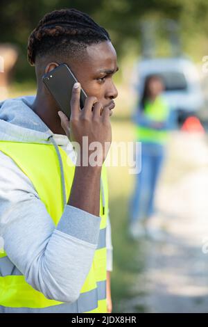 Wütender Mann, der auf einem kaputten Auto sitzt und um Hilfe ruft Stockfoto