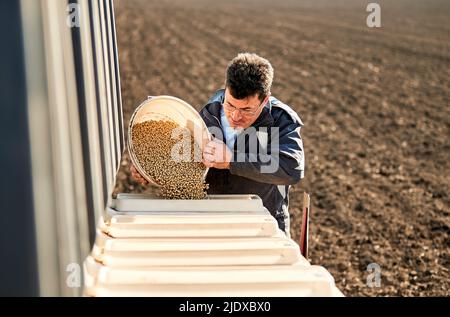 Männlicher Bauer, der Sojabohnensamen in die Maschine auf dem Feld gießt Stockfoto