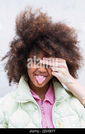 Verspieltes Mädchen, das aus der Zunge ragt, wobei die Hand der Frau ihr Auge bedeckt Stockfoto