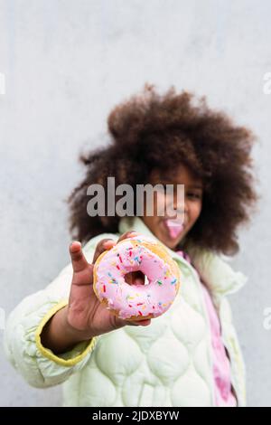 Mädchen hält Donut vor der Wand Stockfoto