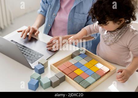 Mutter, die von zu Hause aus mit einem Laptop arbeitet, während ihre Tochter mit Bausteinen spielt Stockfoto