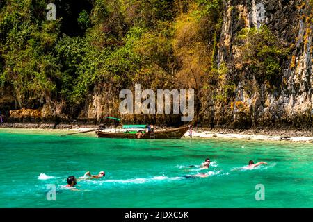 Schwimmer im türkisfarbenen Wasser der thailändischen Phi Phi Inseln. Der Strand und ein großer Felsen sehen aus wie ein Paradies. Stockfoto