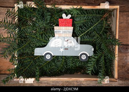 Kiste gefüllt mit Nadelholzzweigen und Weihnachtsdekoration des Weihnachtsmannes, der Geschenke mit dem Auto liefert Stockfoto