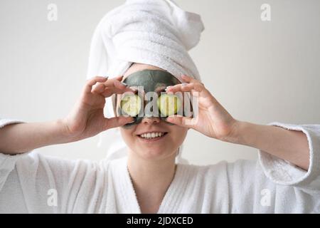 Glückliche Frau, die zu Hause Gurkenscheiben über die Augen hält Stockfoto