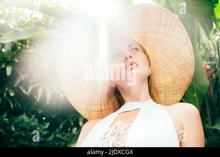 Porträt einer jungen Frau, die Strohhut trägt, beleuchtet vom Sonnenlicht Stockfoto