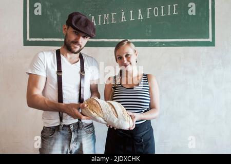 Mitarbeiter halten in der Bäckerei frisch gebackenes Landbrot vor der Wand Stockfoto