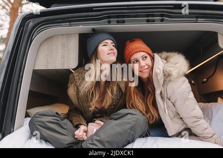 Lächelnde Frauen mit langen Haaren tragen Strickmützen und sitzen im Wohnheim Stockfoto