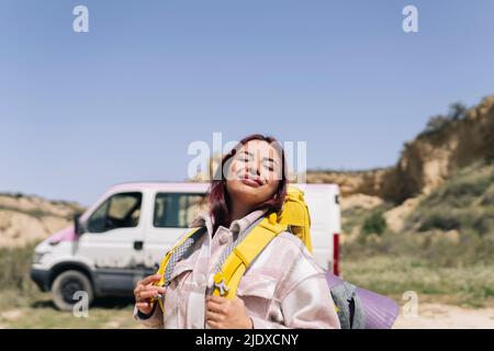 Lächelnde Frau mit Rucksack genießen sonnigen Tag Stockfoto
