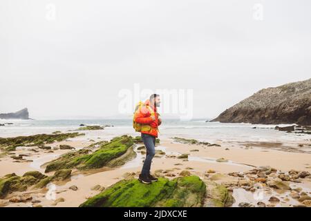 Mann im Rucksack, der am Strand auf Felsen steht Stockfoto