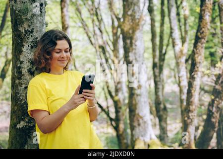 Lächelnde Frau SMS auf Handy im Wald Stockfoto