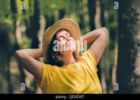 Kontemplative Frau mit Händen hinter dem Kopf, die sich im Wald entspannt Stockfoto