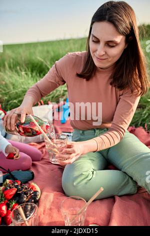 Junge Frau gießt Wasser in Glas auf das Feld Stockfoto