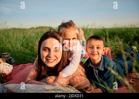 Lächelnde Mutter und Kinder liegen beim Picknick auf dem Feld Stockfoto