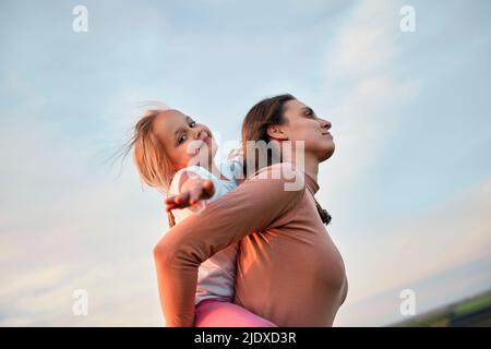 Mutter Huckepack nette Tochter bei Sonnenuntergang Stockfoto