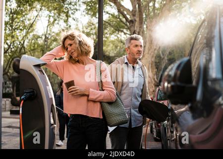 Reifes Paar mit Auto an der Ladestation Stockfoto