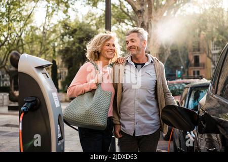 Lächelndes reifes Paar lädt Elektroauto Stockfoto