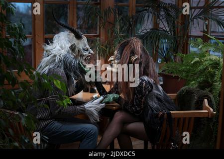 Krampus und Hexe mit Weinglas halten die Hände am Tisch Stockfoto