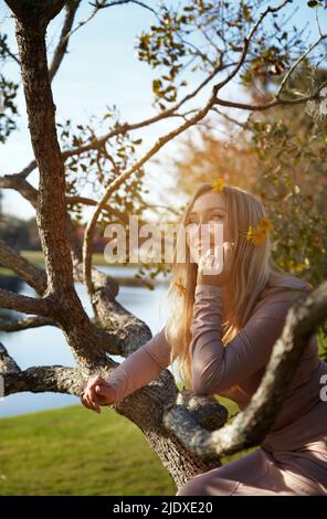 Kontemplative Frau, die sich im Park auf einen Ast des Baumes lehnt Stockfoto