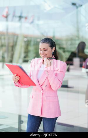Lächelnde Geschäftsfrau beim Lesen von Dokumenten, die über einen Lautsprecher auf dem Mobiltelefon sprechen Stockfoto