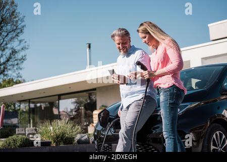 Lächelnder Mann, der der Frau an einem sonnigen Tag das Handy mit dem Stecker zeigt Stockfoto