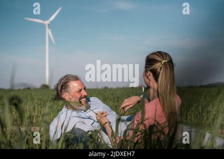 Glücklicher Mann mit Frau, die auf dem Feld sitzt Stockfoto
