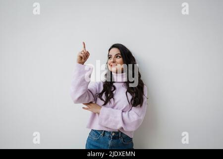 Lächelnde junge, schöne Frau, die vor einer weißen Wand zeigt Stockfoto