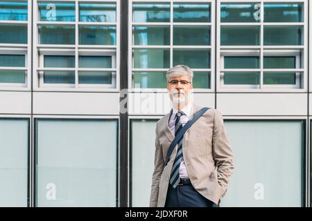 Lächelnder Geschäftsmann mit Brillen, der vor dem Gebäude steht Stockfoto