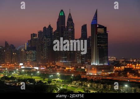 Vereinigte Arabische Emirate, Dubai, beleuchteter Golfplatz bei Nacht mit den Jumeirah Lakes Towers im Hintergrund Stockfoto