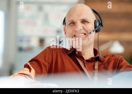 Glücklicher Geschäftsmann, der im Büro ein Headset trägt Stockfoto