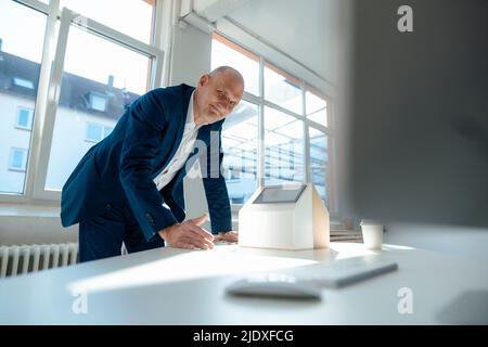 Lächelnder leitender Ingenieur mit Solarmodul im Modellhaus im Büro Stockfoto