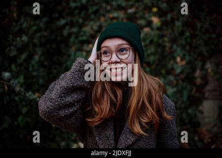 Fröhliche Rothaarige Frau mit Brille und Strickmütze im Park Stockfoto