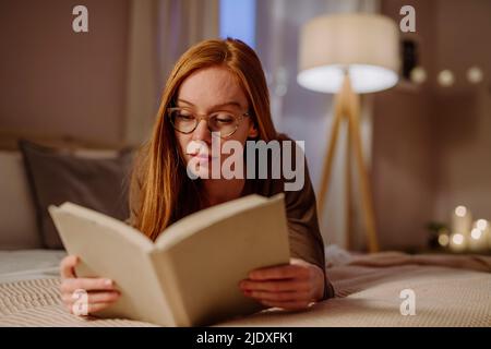 Frau, die zu Hause auf dem Bett liegt, liest ein Buch Stockfoto