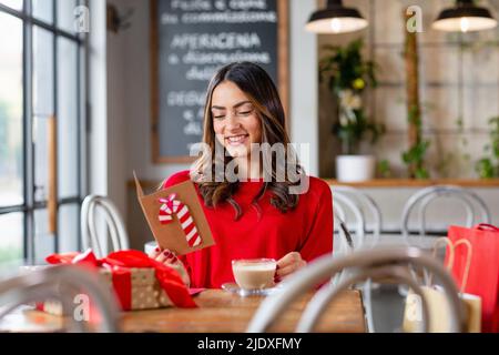 Glückliche schöne Frau beim Lesen der Weihnachtskarte im Café Stockfoto