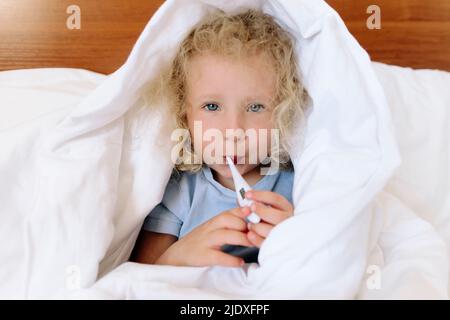Kranke Mädchen in Decke mit Digitalthermometer gewickelt zu Hause Stockfoto