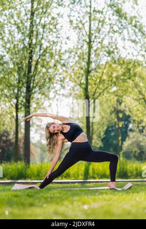 Lächelnde junge Frau, die Yoga macht, während der Arm auf der Wiese angehoben wird Stockfoto