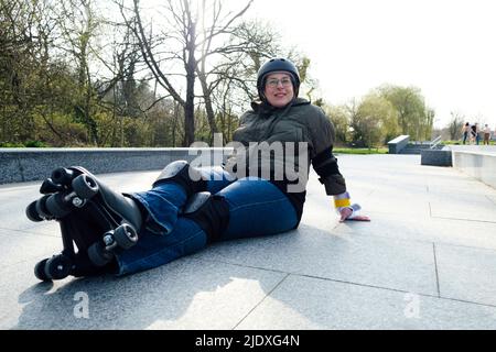 Frau, die sich auf dem Fußweg mit Rollschuhen im Park ausruht Stockfoto